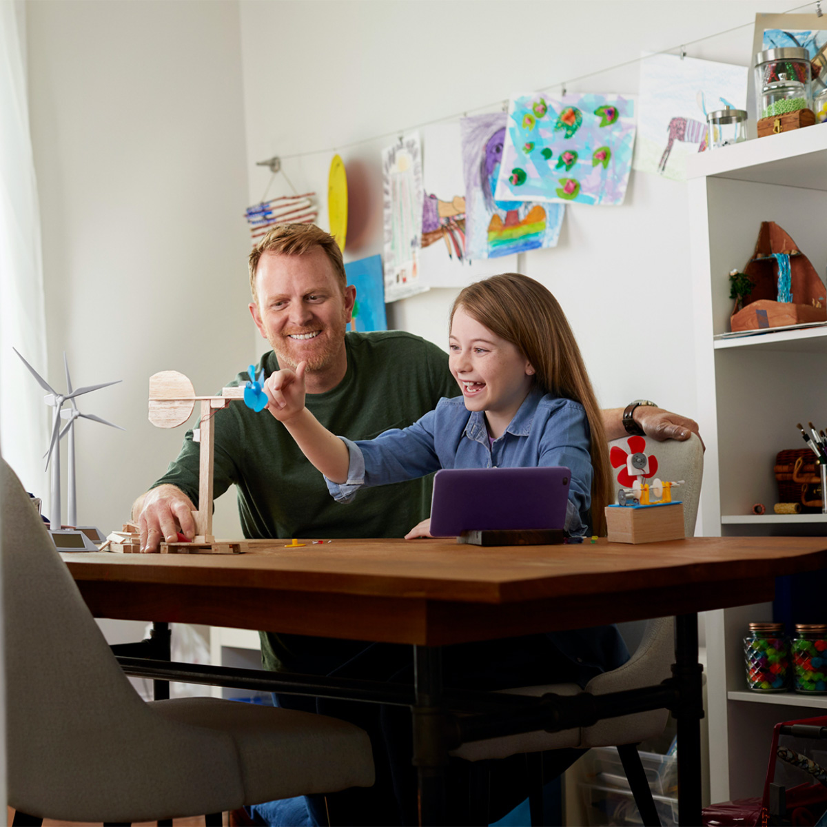 A Father and daughter sit at a table together and work on a science project