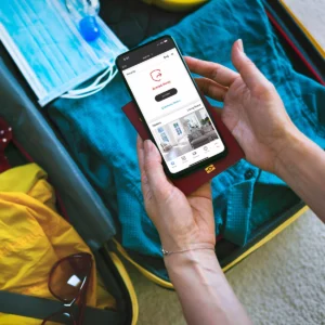 An individual opening up their luggage case while traveling, and checking on the status of their home using the Total Connect App to see through the cameras they have installed.